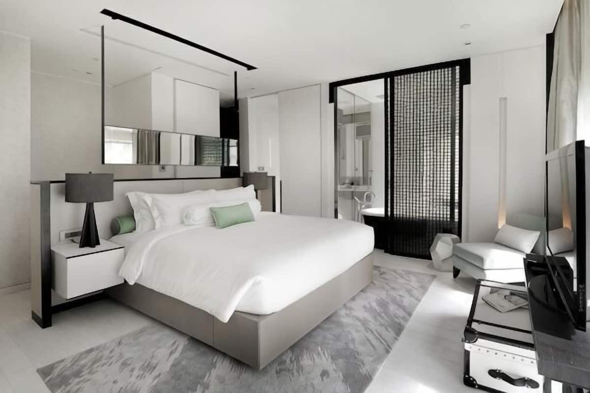 Quarto moderno com uma cama grande, mesas de cabeceira, uma televisão e um banheiro visível por uma porta aberta.