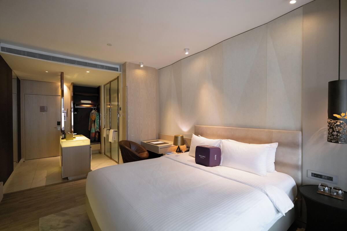 A modern hotel room with a large bed, a desk, a chair, a vanity, and a walk-in closet.