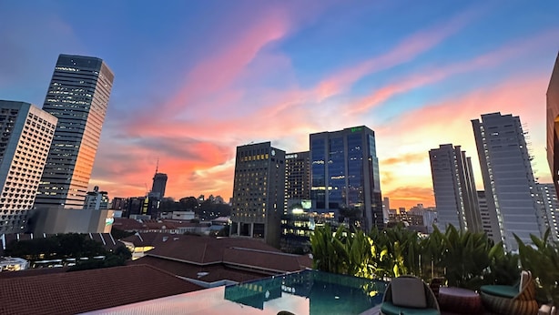 Una piscina en la azotea con sillones de descanso y un horizonte urbano al atardecer.