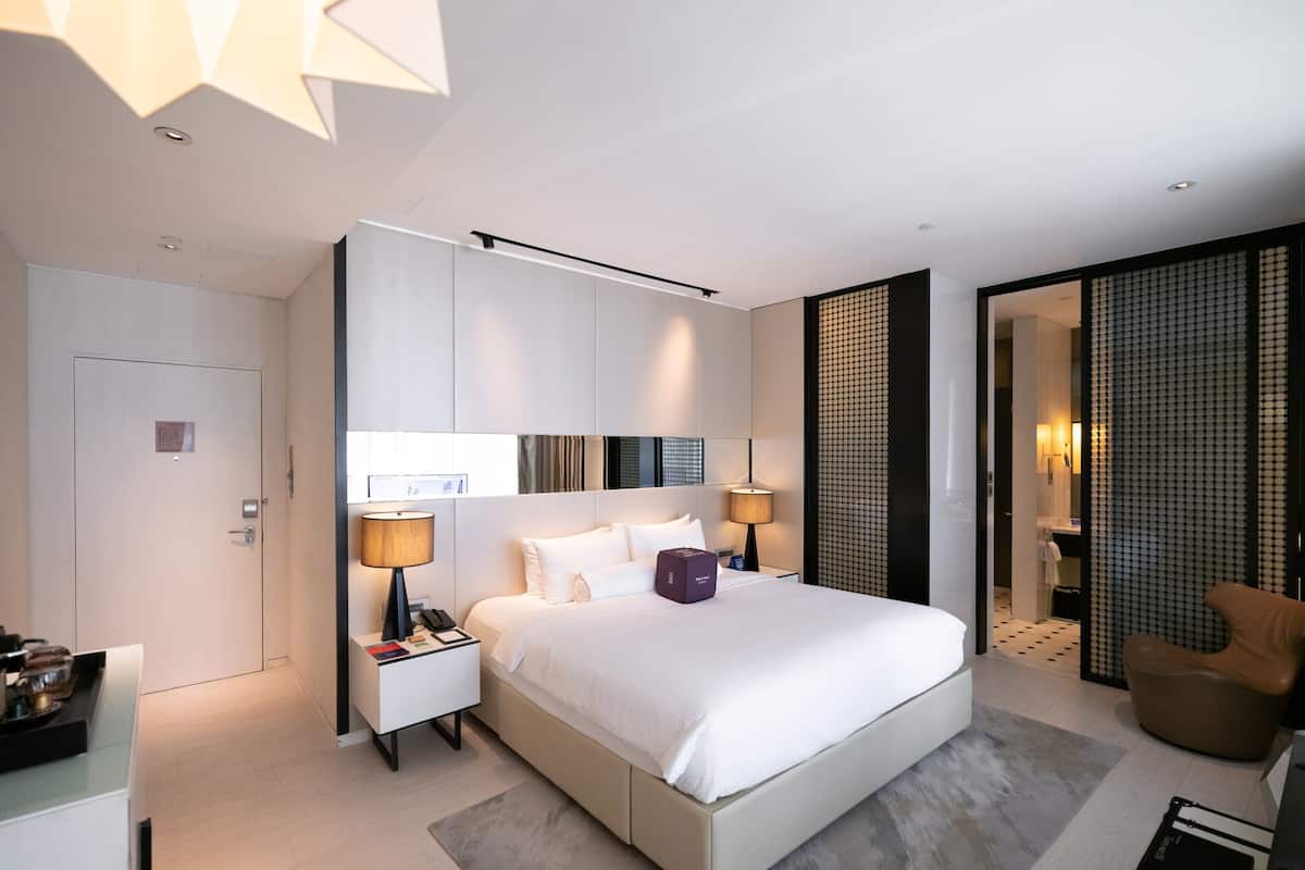 A modern hotel room with a large bed, bedside lamps, a desk, and a chair.