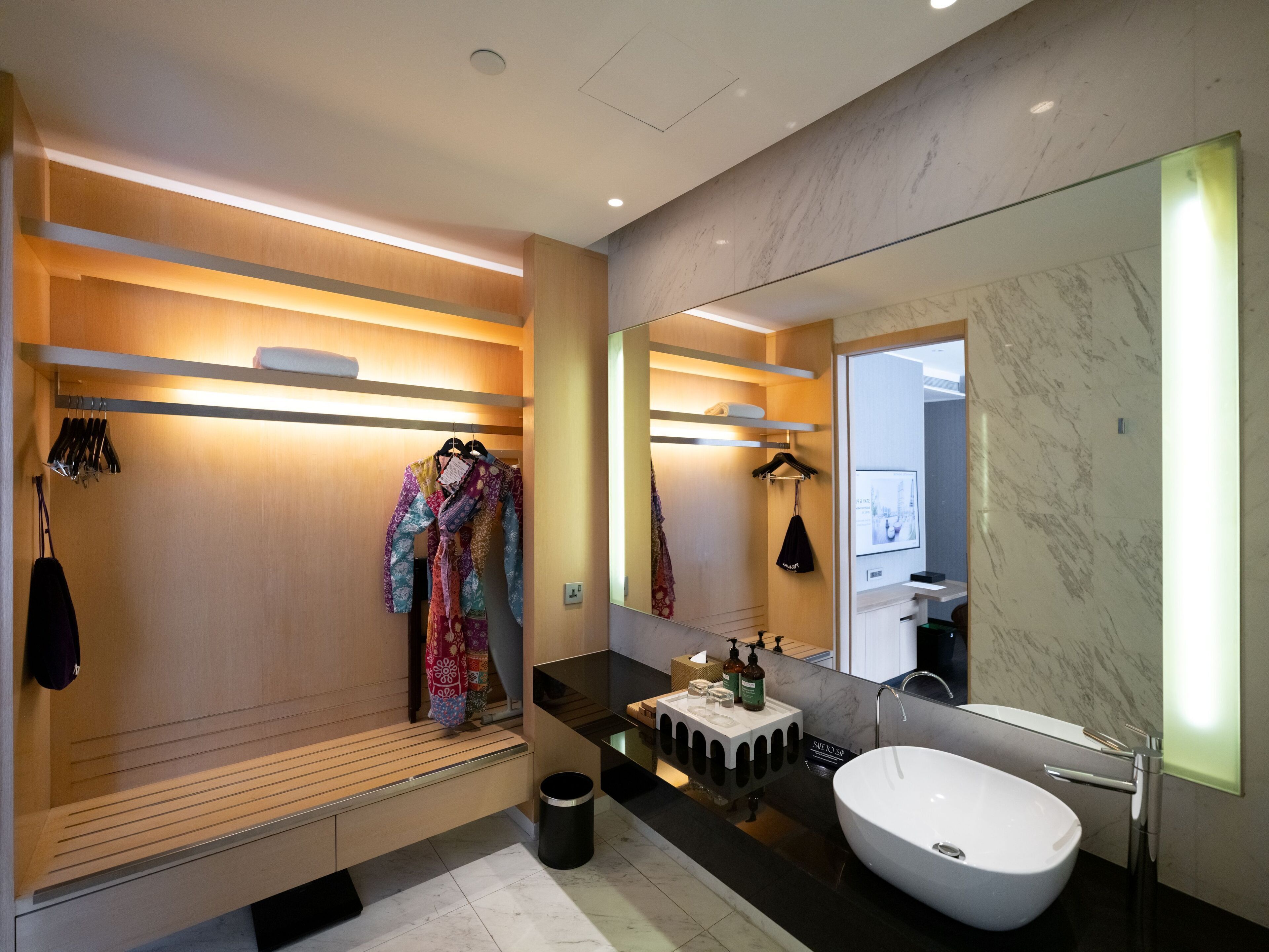Un baño moderno con un espejo grande, una bañera independiente y un mueble de tocador de madera con encimera negra.