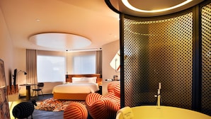 Una habitación de hotel con una cama grande, una bañera, un escritorio con lámpara y un papel tapiz decorado.