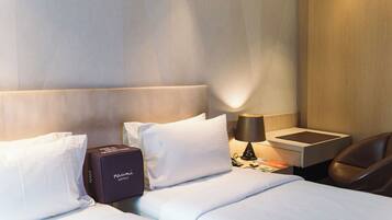 Habitación de hotel con cama, almohadas, mesita de noche con lámpara, una silla y minibar.