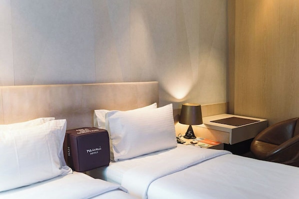 A hotel room with a neatly made bed, a bedside table with a lamp, a black box with the hotel name, and a leather chair. - Naumi Hotel Singapore (Singapore)