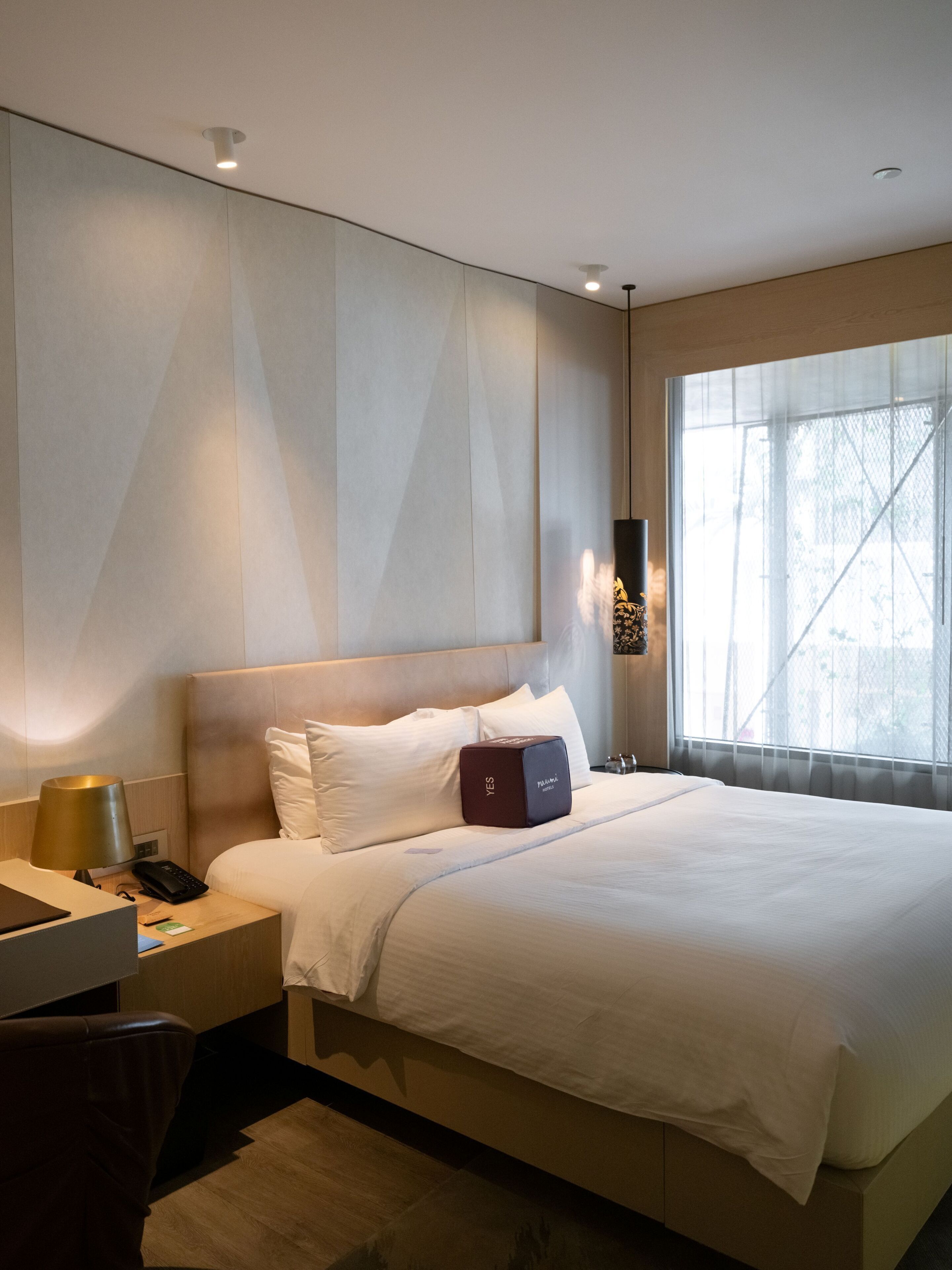 A hotel room with a bed, bedside table, lamp, and a window with a view.