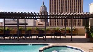 A rooftop pool with a hot tub, outdoor seating, and a view of a tall building in the background.