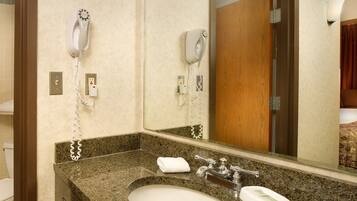 Une salle de bain dotée d’un comptoir en granit, d’un lavabo, d’un miroir et de deux sèche-cheveux fixés au mur.
