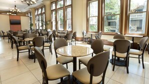 Un comedor amplio con múltiples mesas y sillas, ventanas grandes con vistas al exterior y una lámpara de araña moderna.