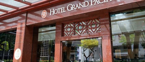 The exterior of Hotel Grand Pacific with a modern glass facade and a red metal framework.