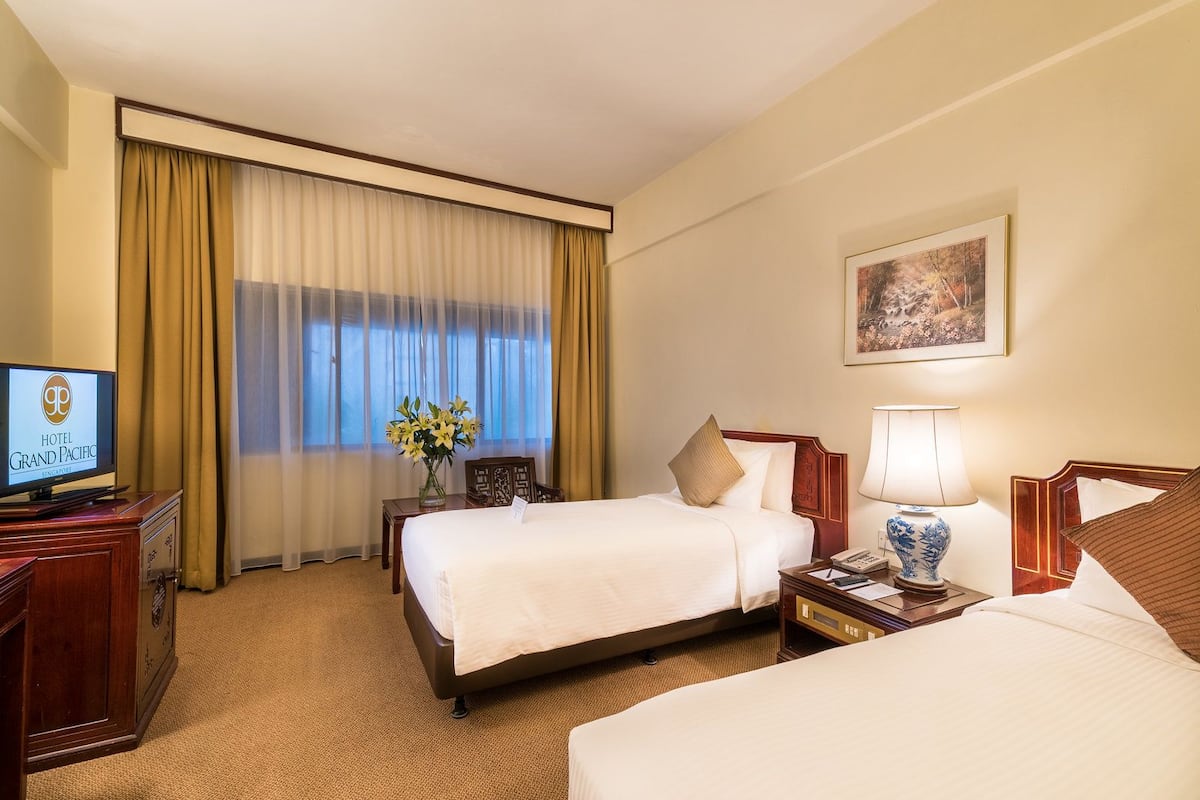 A hotel room with two beds, a desk with a computer, a lamp, and a painting on the wall.