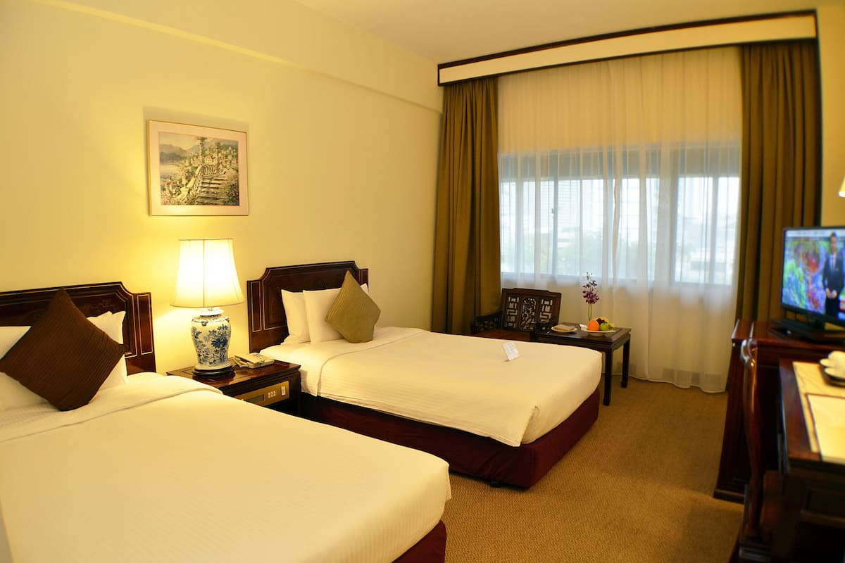 A hotel room with two beds, a television, a desk with a lamp, and a window with curtains.