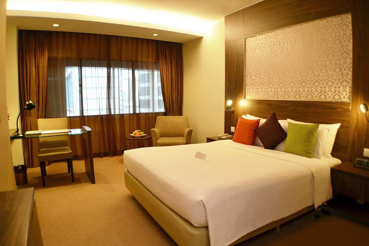 A hotel room with a large bed, a desk, a chair, and a view of the city through the window.