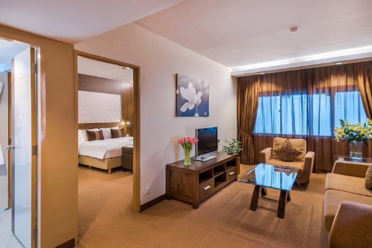 A hotel room with a bed, a TV, a glass coffee table, and a sofa.