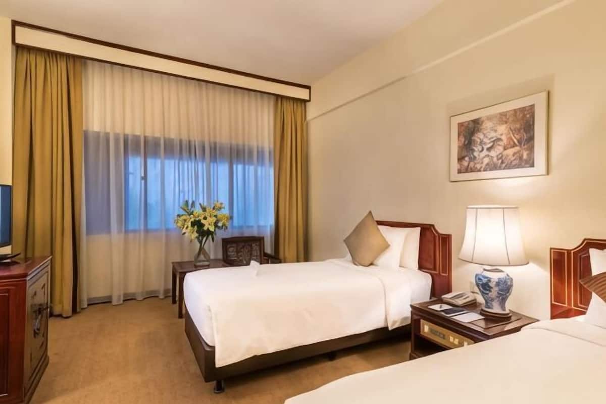 A hotel room with a bed, bedside tables, a lamp, a painting on the wall, and a window with curtains.