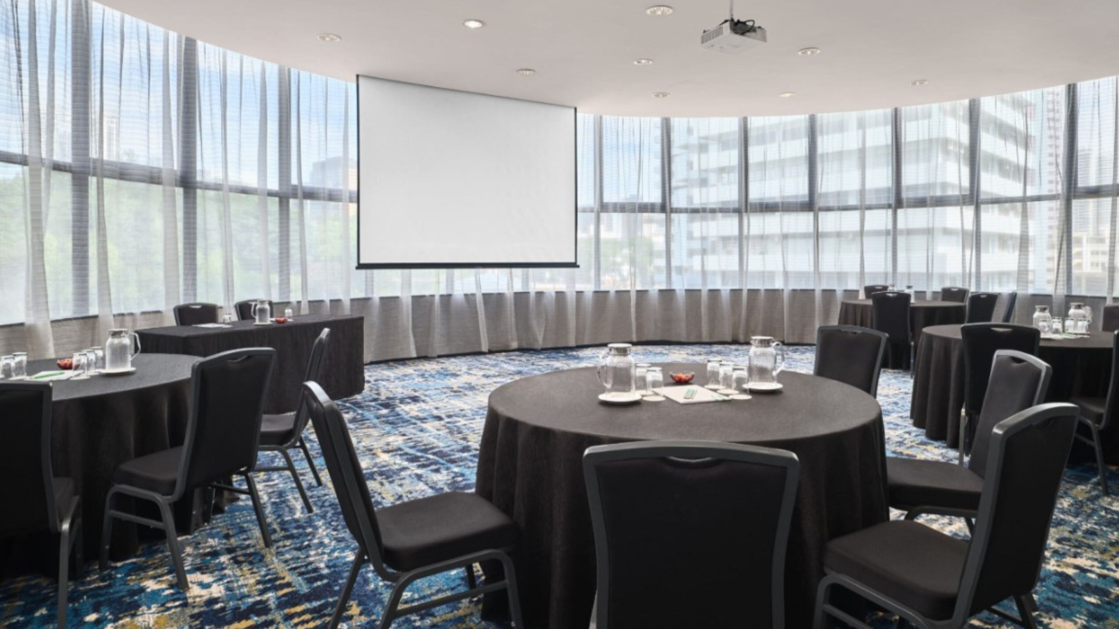 A conference room with round tables, black chairs, and a large screen.