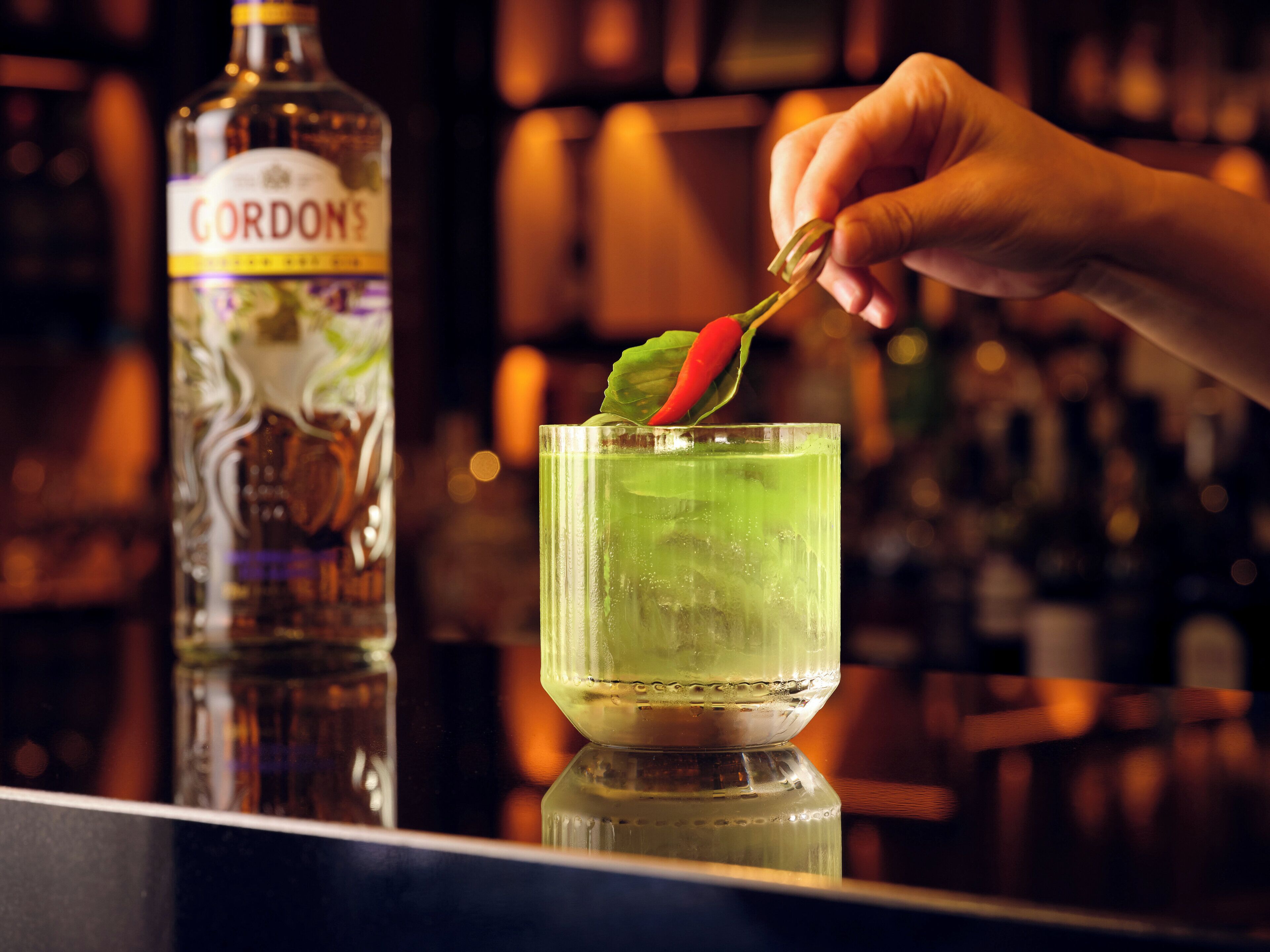 Un bar, avec une bouteille de CORDONS et une main en train de décorer un verre.
