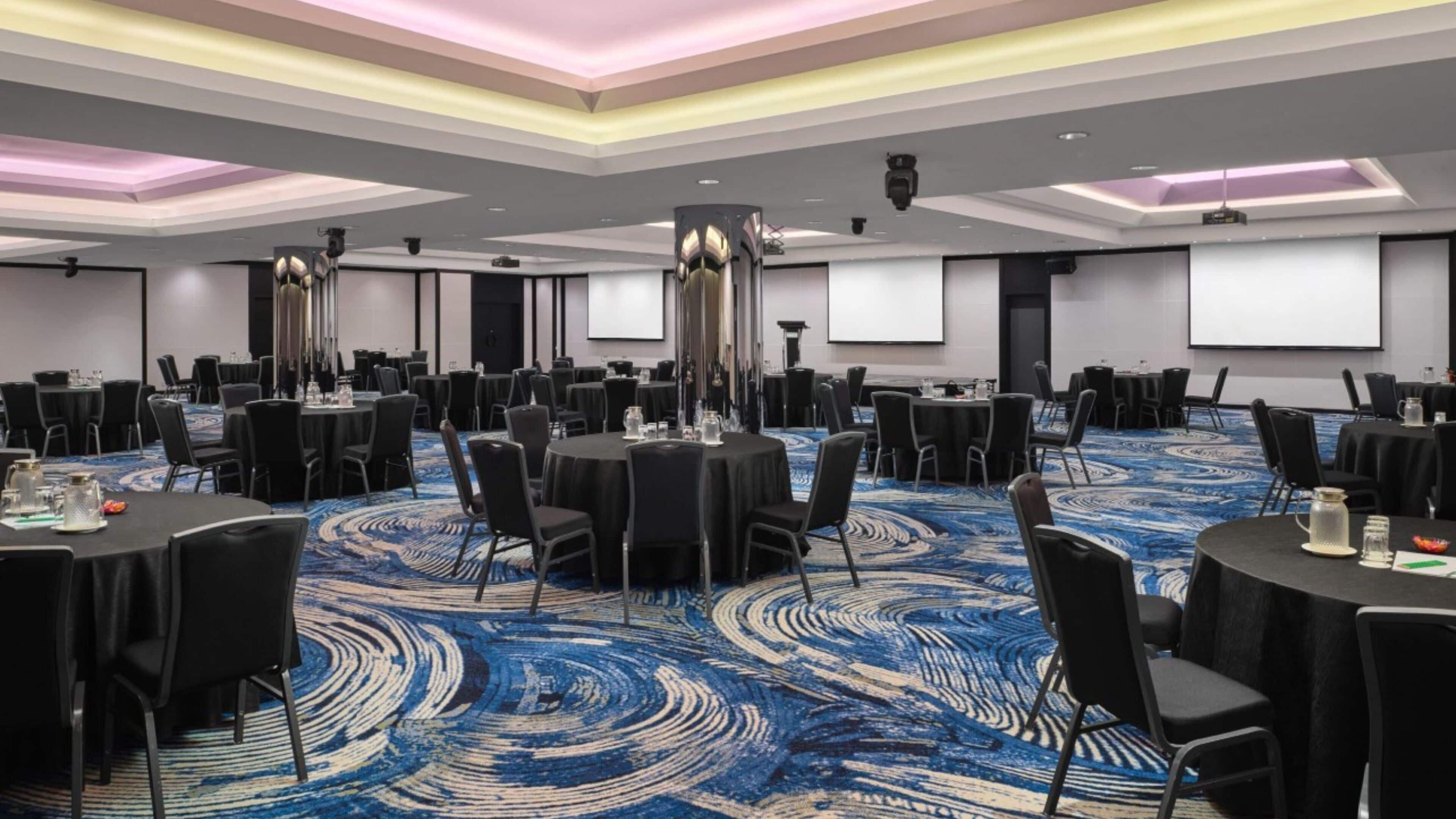A conference room with round tables, black chairs, and a blue patterned carpet.