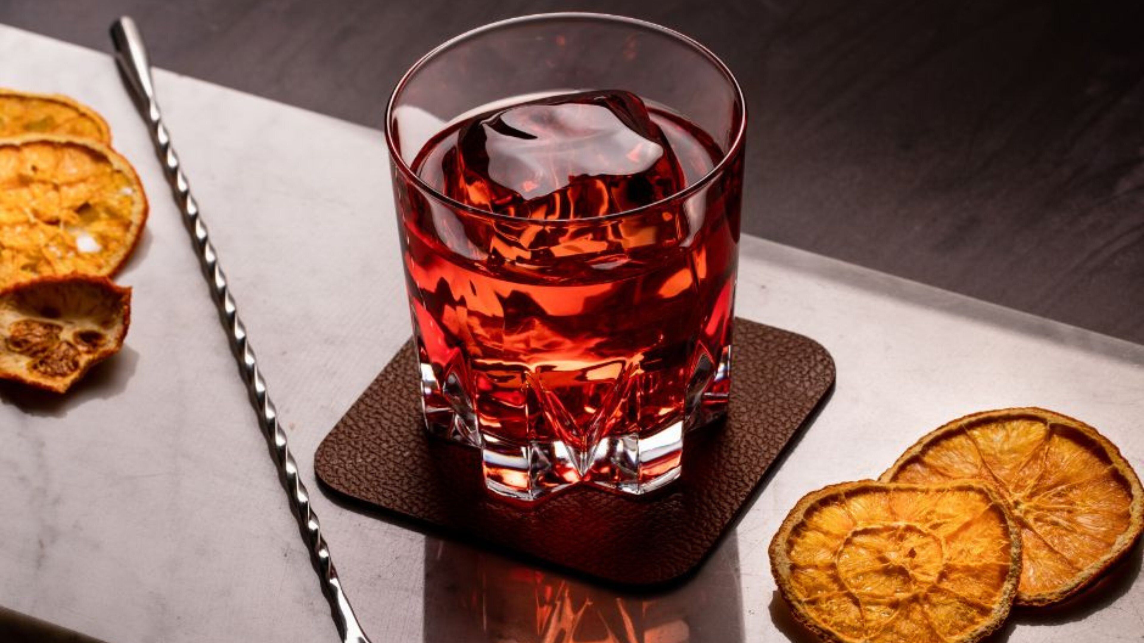 A glass of red beverage on a coaster with a metal straw and dried orange slices beside it.