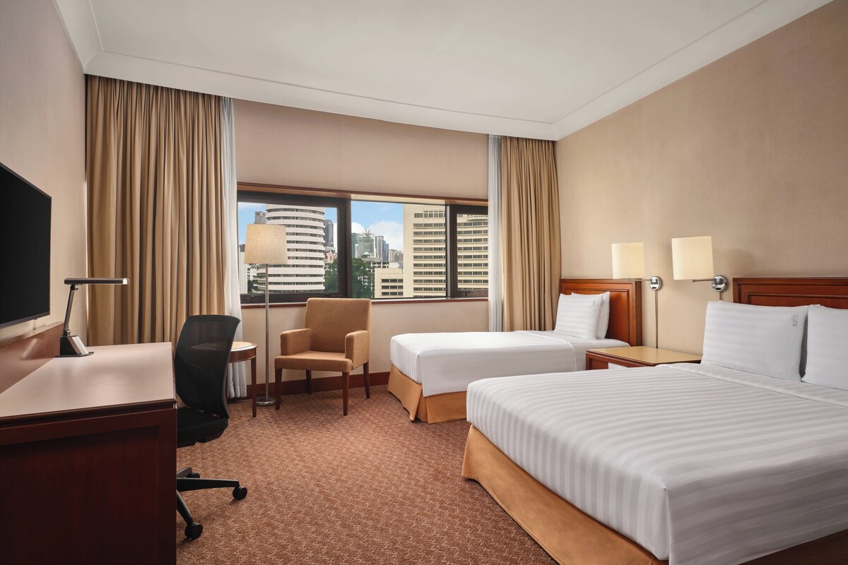 A hotel room with two beds, a desk, a chair, and a TV.
