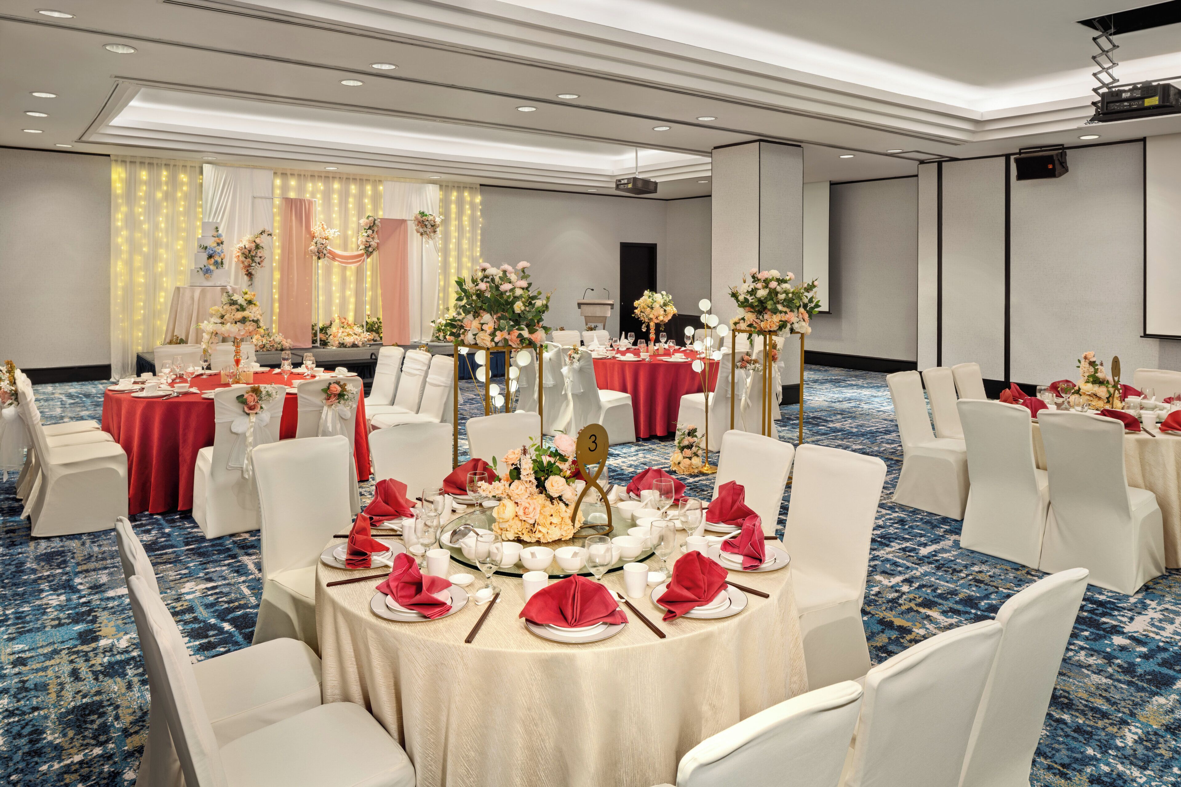 A banquet hall with round tables, white chairs, and red tablecloths.
