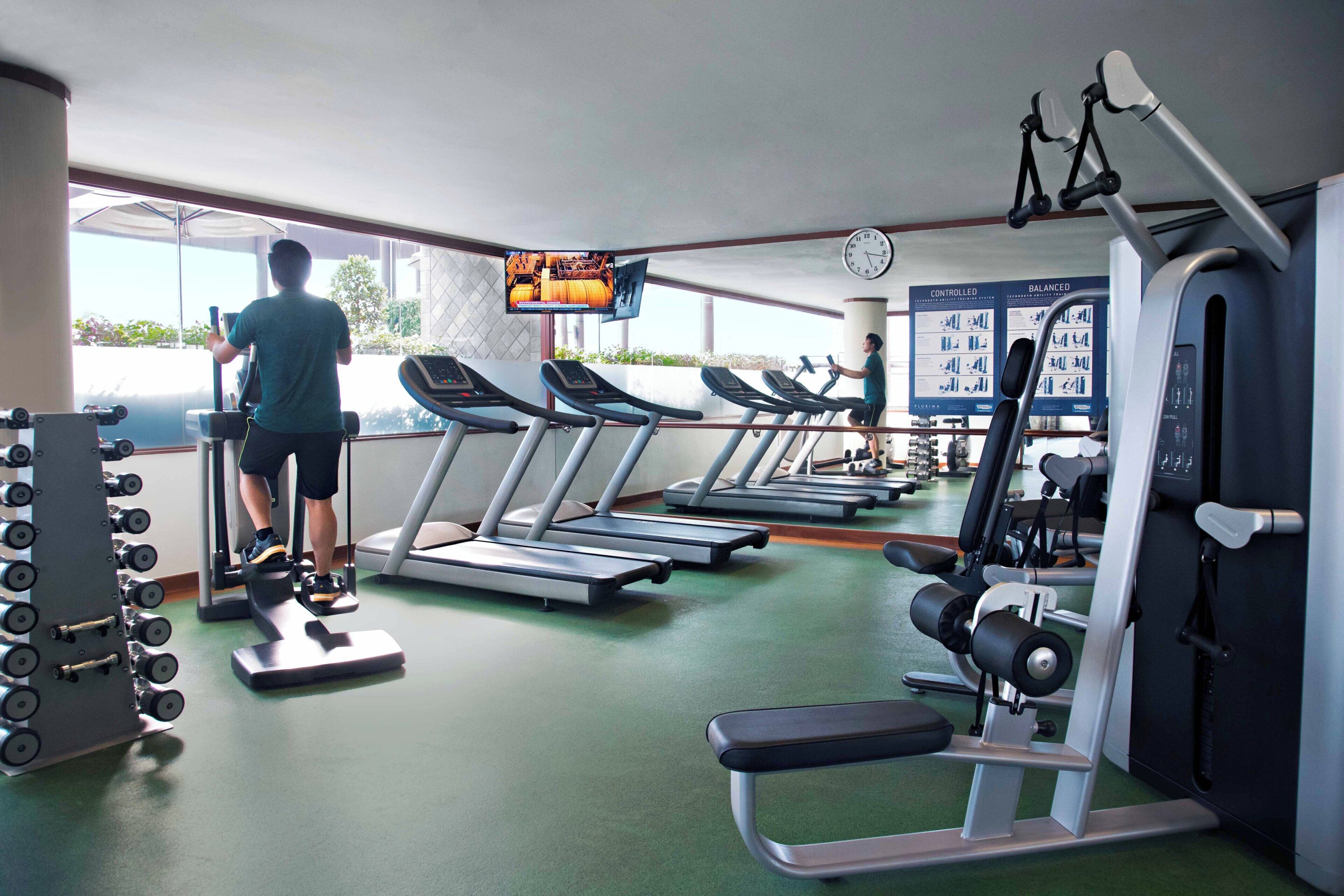 A gym with treadmills, weight machines, and a TV screen displaying a program.