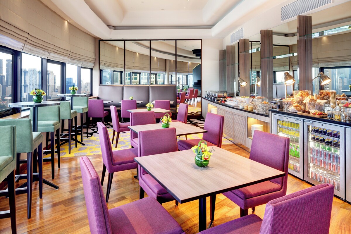 A modern restaurant with purple seating, a bar area, and a view of the city skyline.