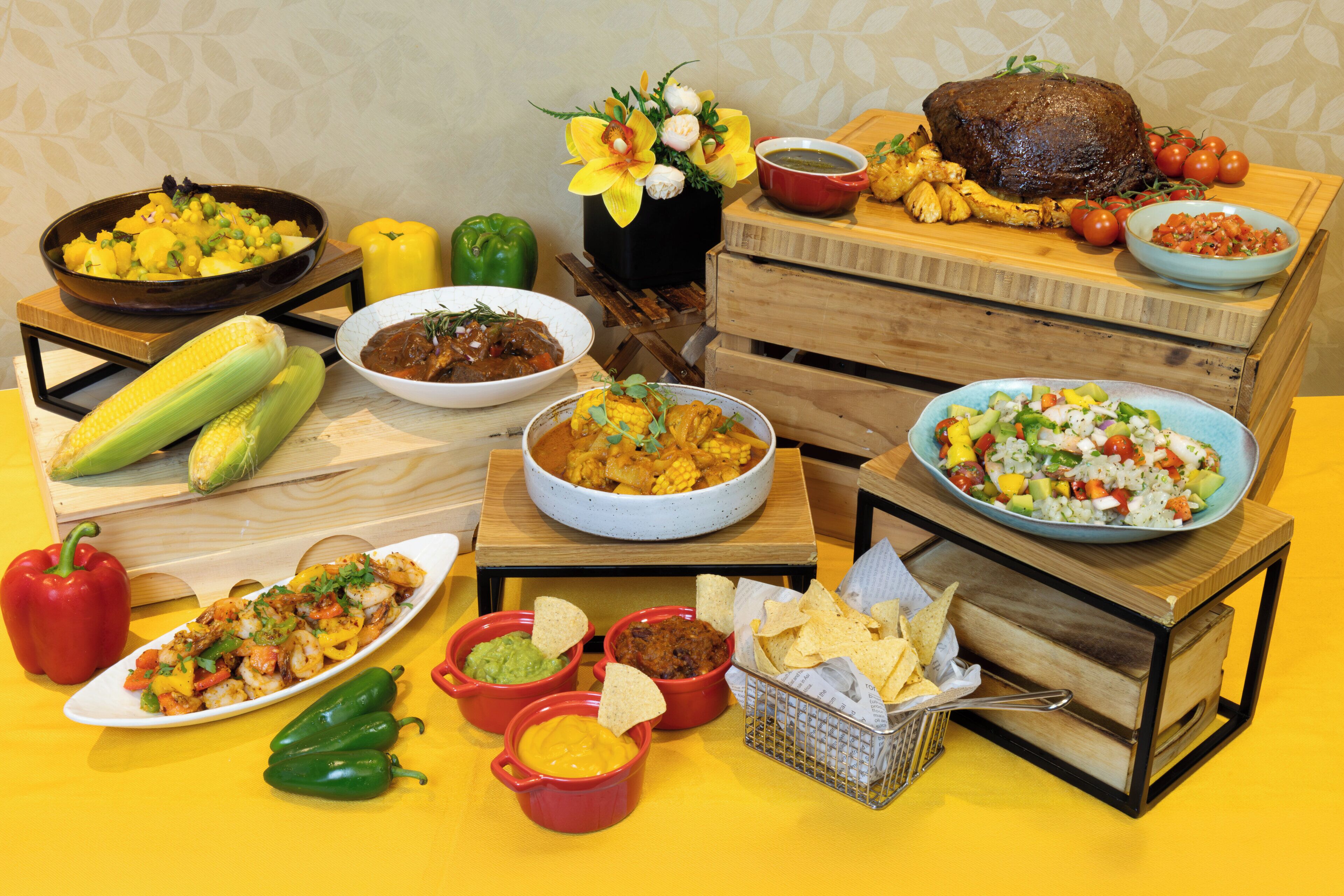 Una mesa con diversos platos, incluyendo una pieza grande de carne asada, mazorcas de maíz y varios recipientes de salsas.