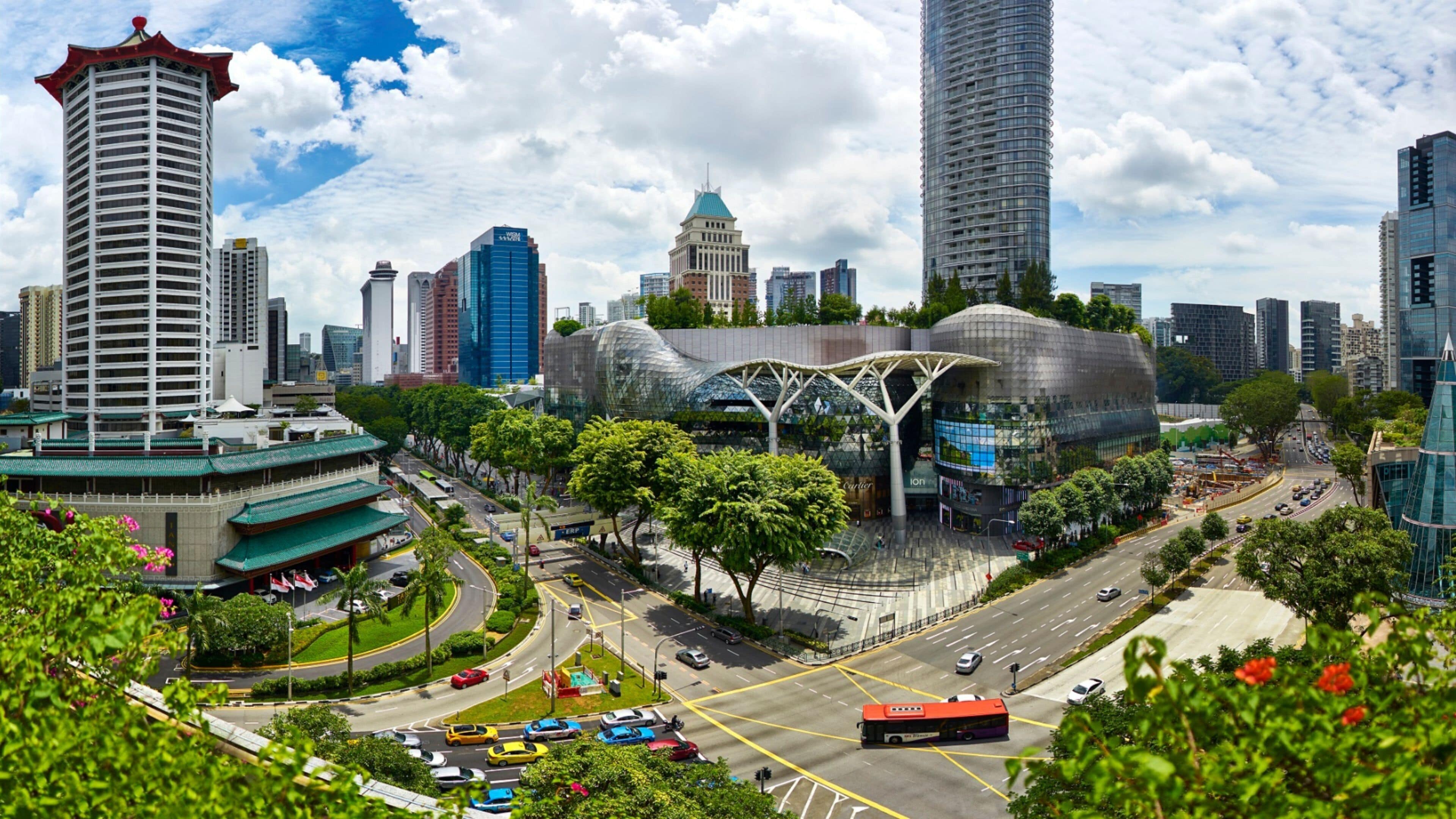 A cityscape with modern buildings, a curved glass structure, and a busy intersection with cars and a bus.