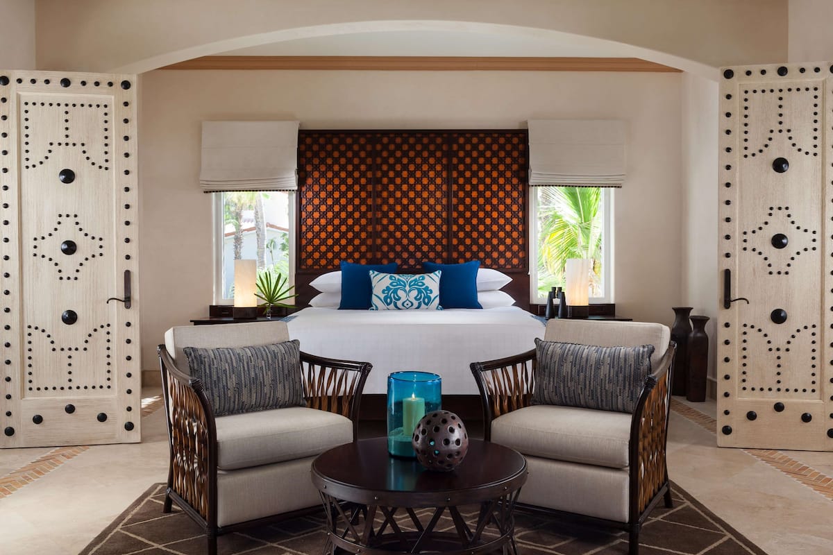 A hotel room with a bed, two armchairs, a round table, and a decorative wall panel.
