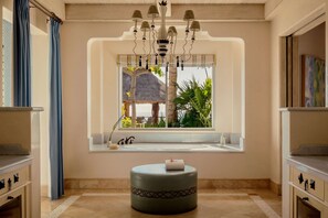 A room with a bathtub window, a round ottoman, and a chandelier.