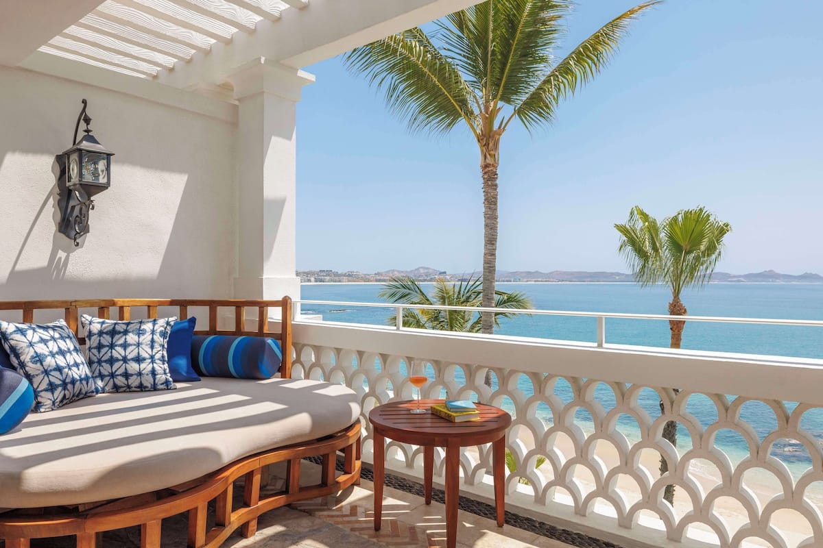 A balcony with a wooden sofa, a small table, and a view of the sea.