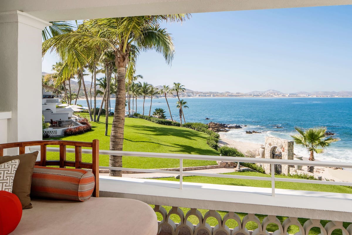 A balcony with a view of the beach, palm trees, and a clear sky.