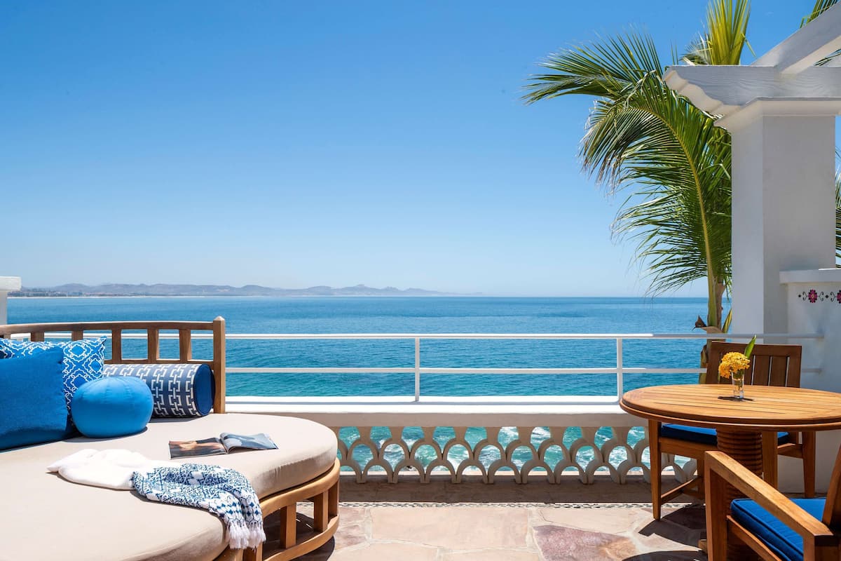 A balcony with a view of the sea, a wooden sofa, a round table, and a white railing.