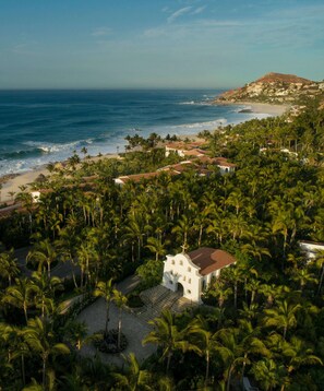 A coastal property with a white building surrounded by palm trees, a beach, and ocean views.