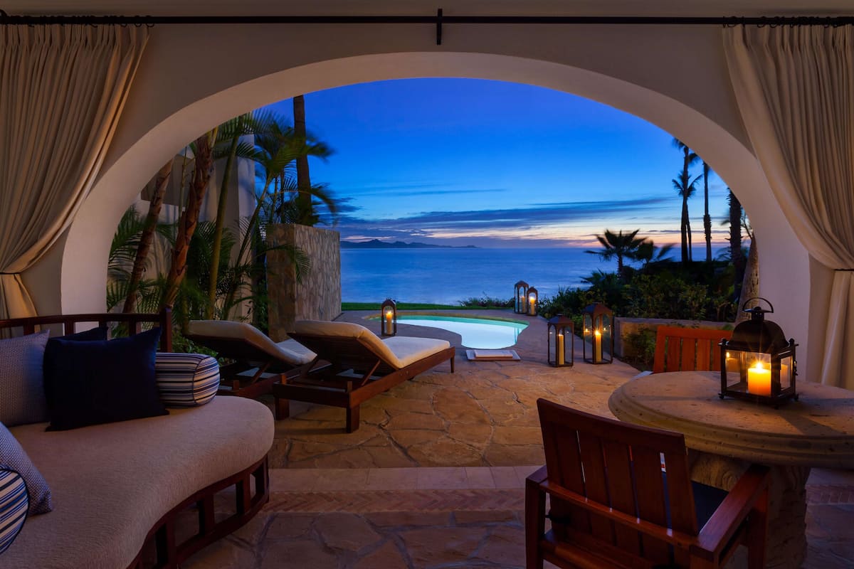 An outdoor seating area with a pool, lounge chairs, and a view of the ocean at dusk.