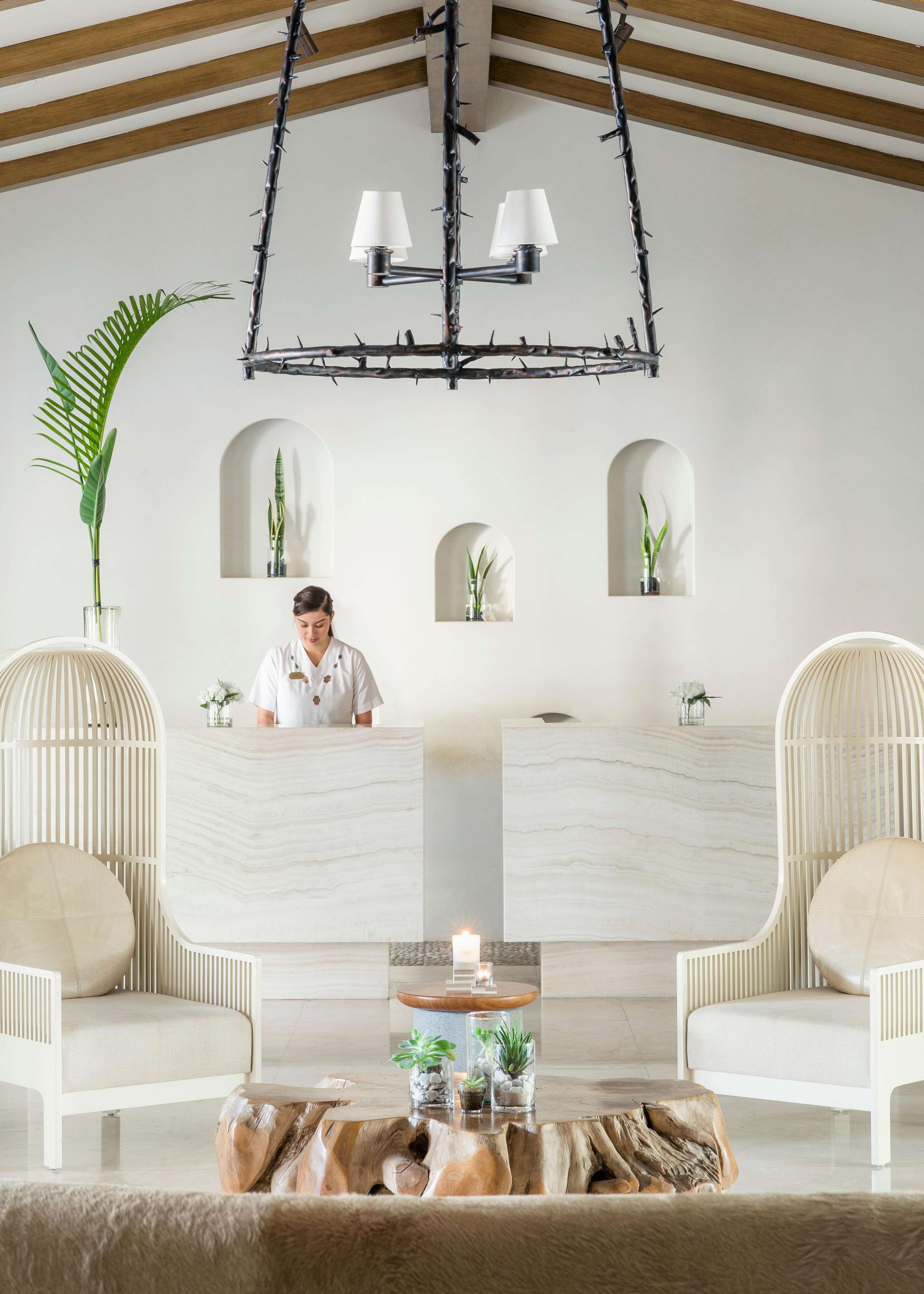 A modern interior with a reception desk, two seating areas, a wooden ceiling, and a chandelier.