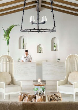 A modern interior with a reception desk, two seating areas, a wooden ceiling, and a chandelier.