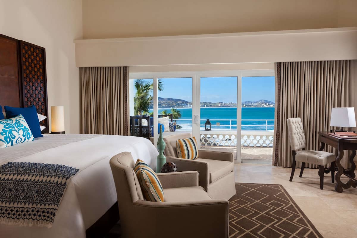 A hotel room with a bed, a sofa, a chair, a desk, and a view of the ocean.