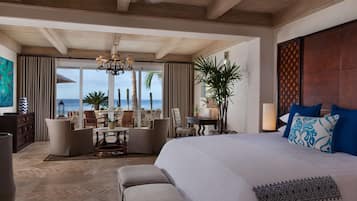Une chambre d’hôtel avec un grand lit, une vue sur l’océan, un coin repas et un ventilateur de plafond.