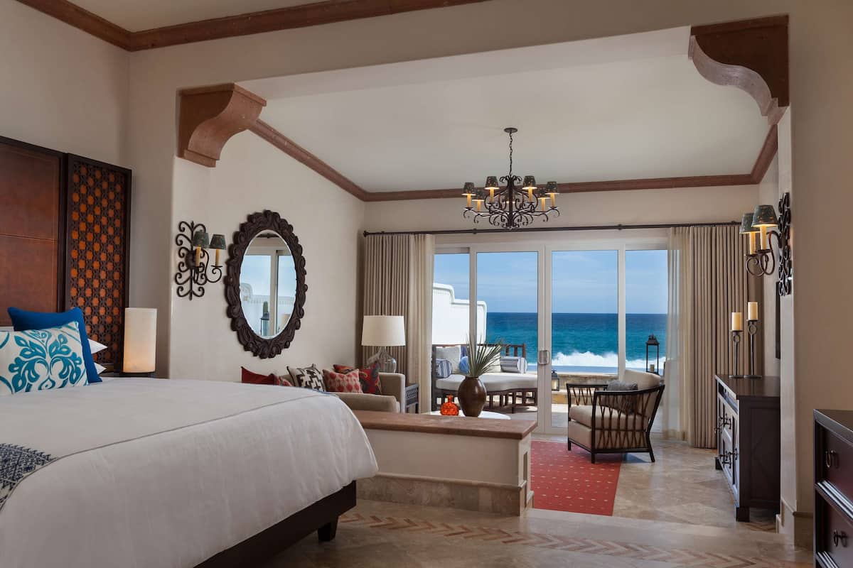 A hotel room with a large bed, a seating area with a view of the ocean, and a chandelier.