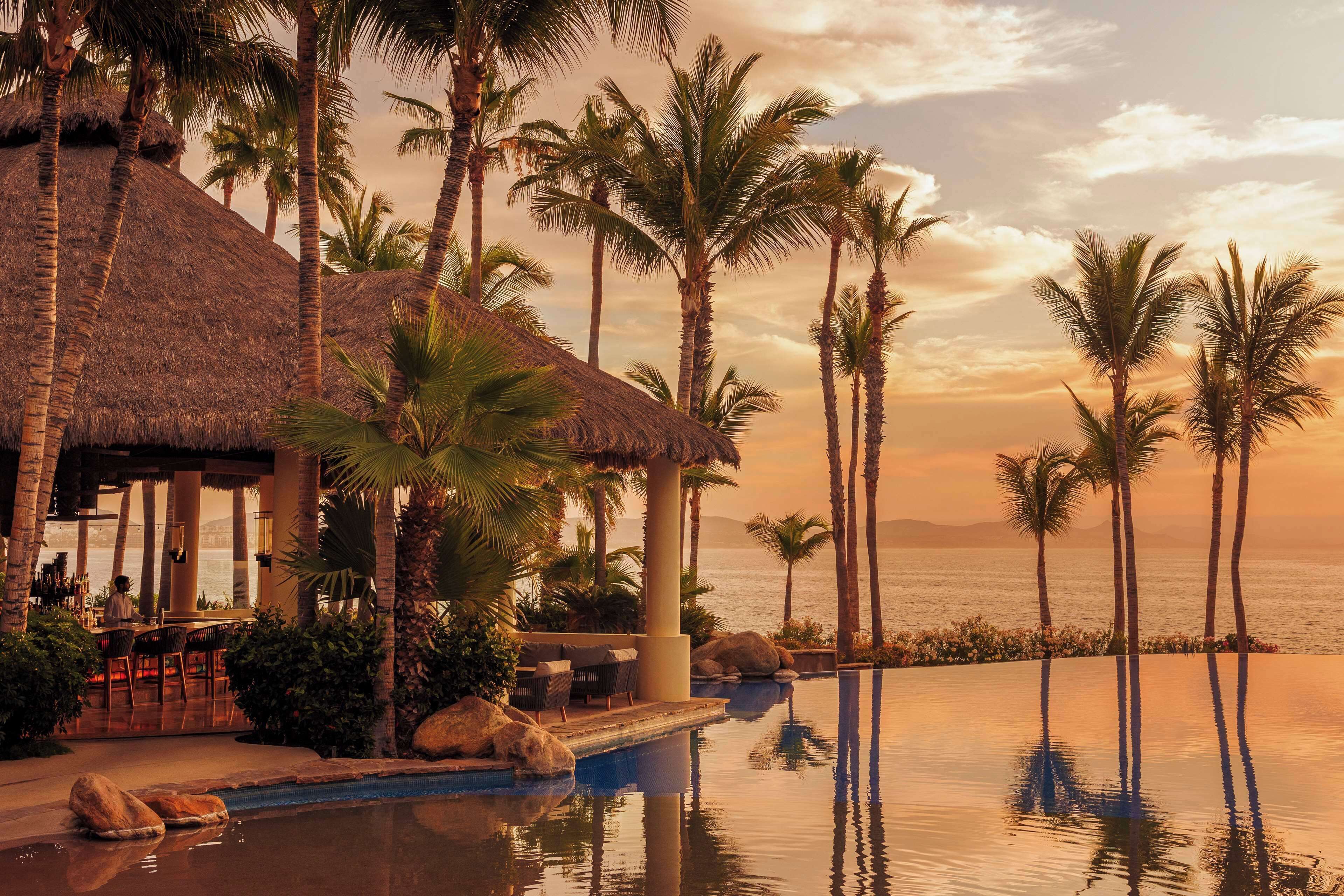 Ein Resort mit Pool, Palmen und einem Gebäude mit Reetdach.