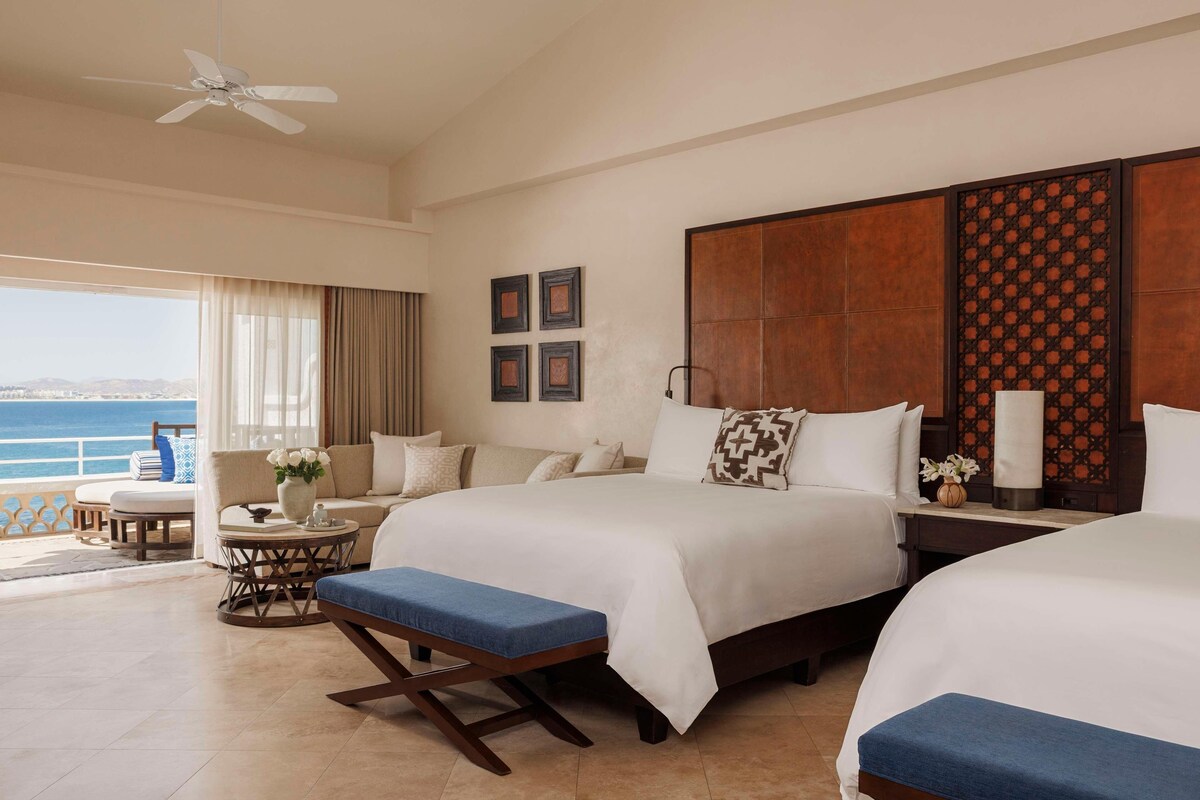 A hotel room with two beds, a balcony with a view, a ceiling fan, and a decorative wall panel.