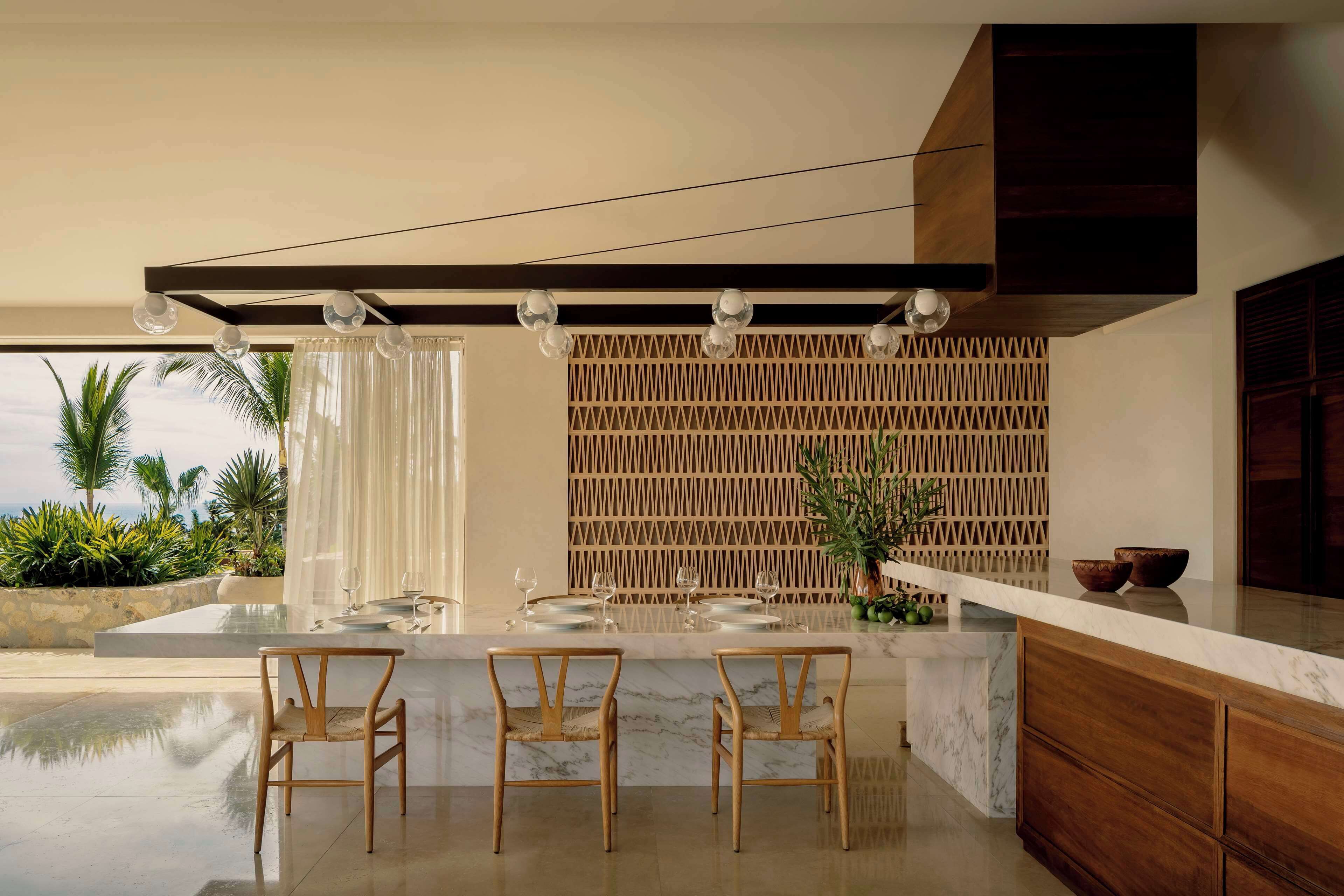 A modern kitchen with a marble countertop, wooden chairs, and a decorative wooden panel.