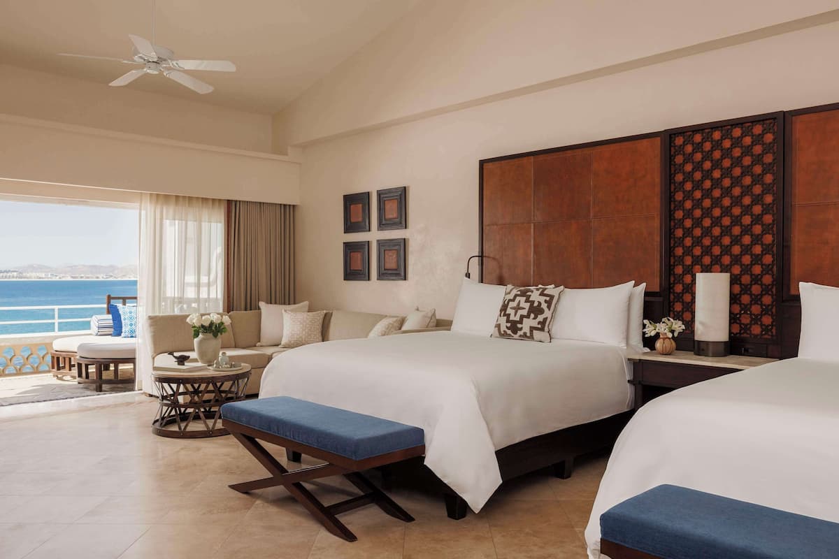 A hotel room with a balcony, a bed, a sofa, a small table, and a bench.