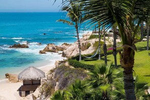 A beach with a thatched-roof hut, palm trees, and a hammock.