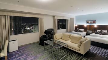 Habitación de hotel con vista a la ciudad, un sofá, una cama, una mesita de vidrio y un sillón de masaje.