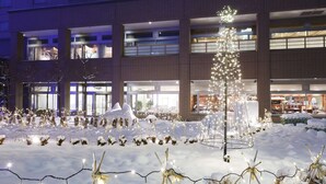 A hotel with multiple floors, large windows, and a snowy outdoor area with string lights and snow-covered plants. - Sapporo Excel Hotel Tokyu (Sapporo)