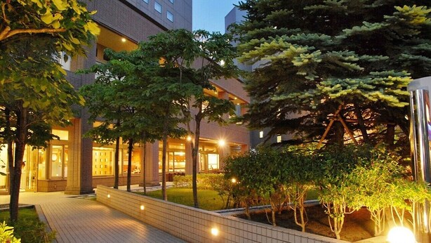 A hotel courtyard with a paved walkway, trees, and a building with multiple floors and balconies. - Sapporo Excel Hotel Tokyu (Sapporo)