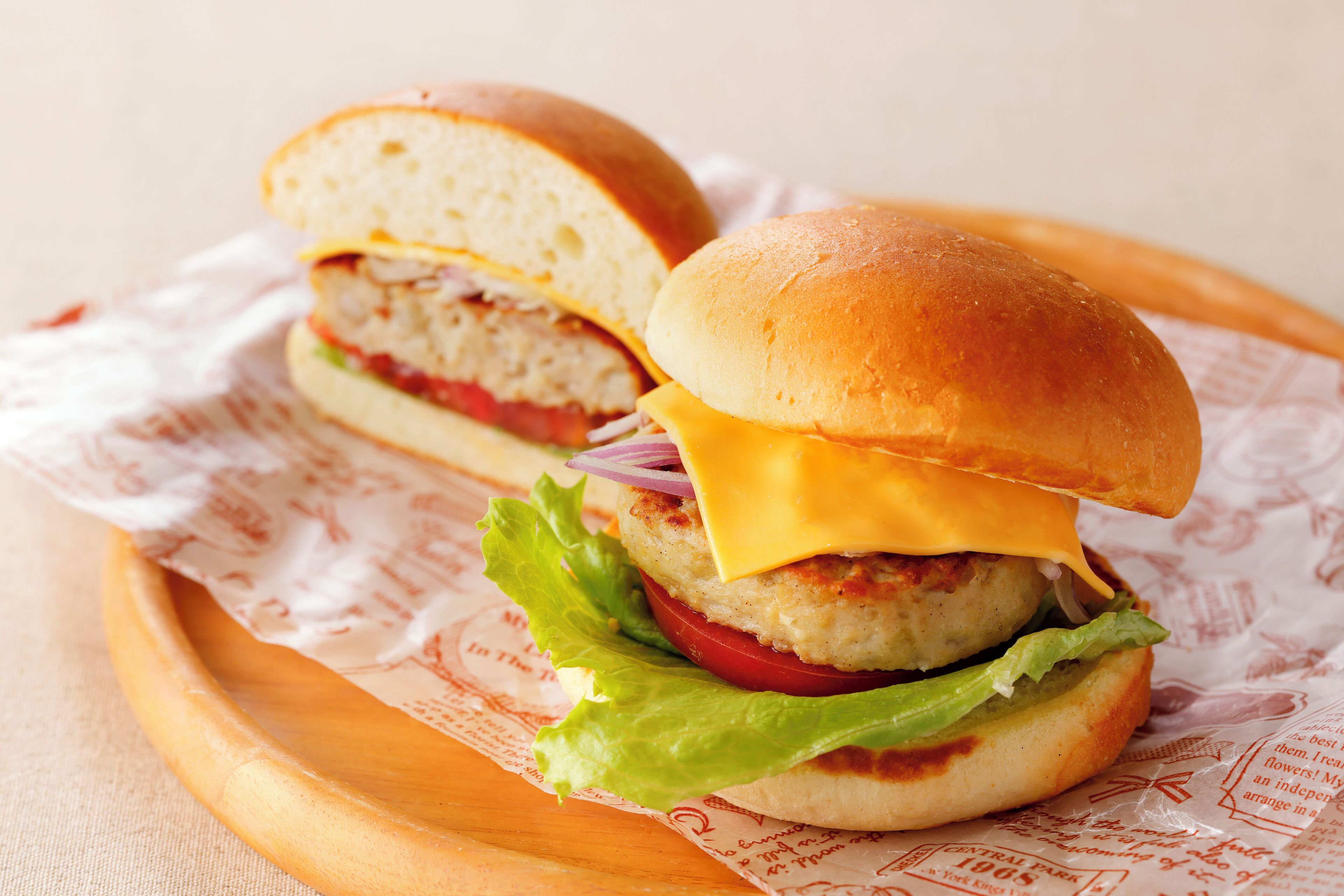 Un hamburger servi sur un plateau en bois, avec un pain, de la laitue, une tomate et du fromage.