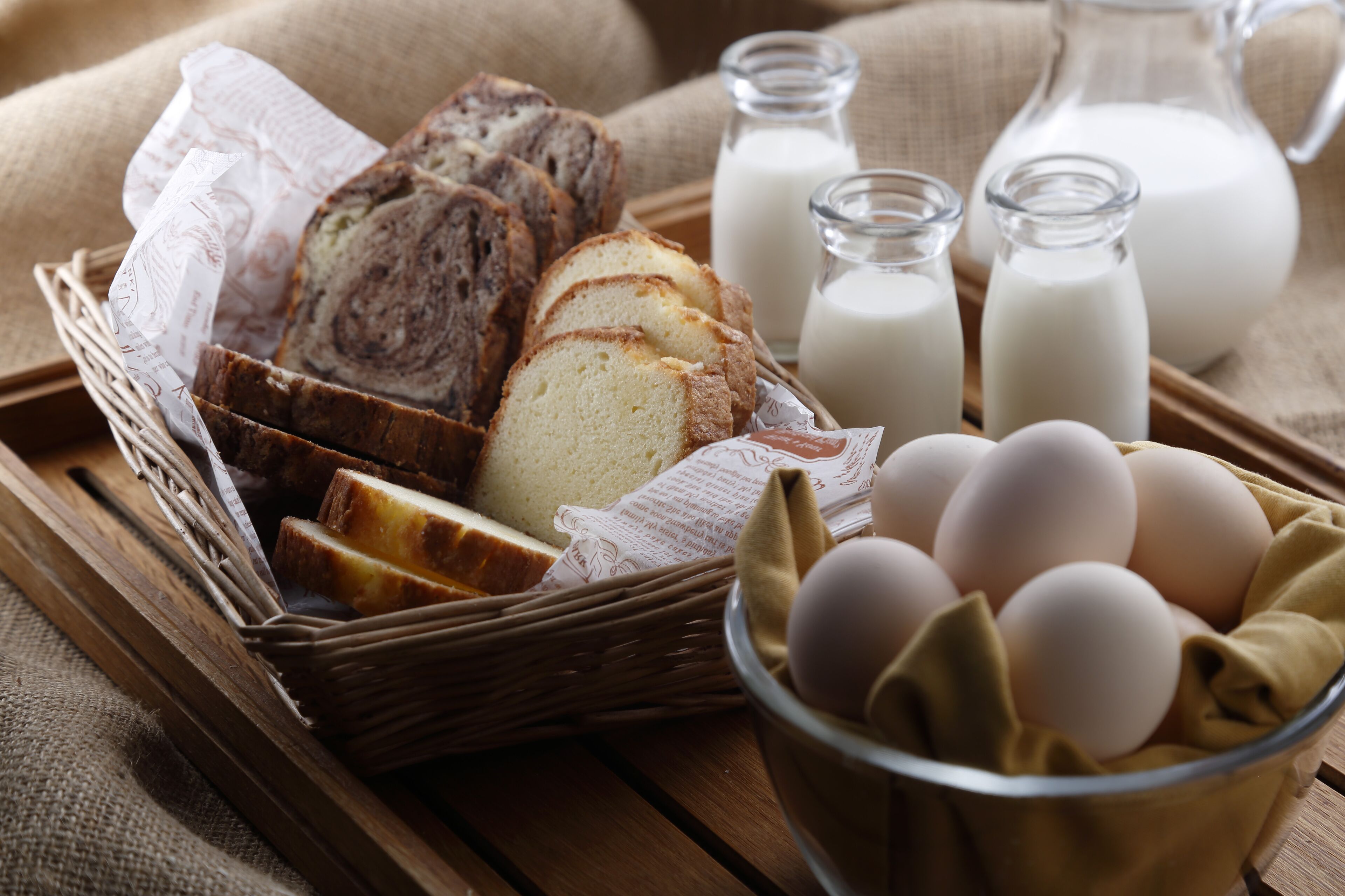 Ein Korb mit Brotscheiben, Eiern und Milchflaschen auf einem Holztablett.